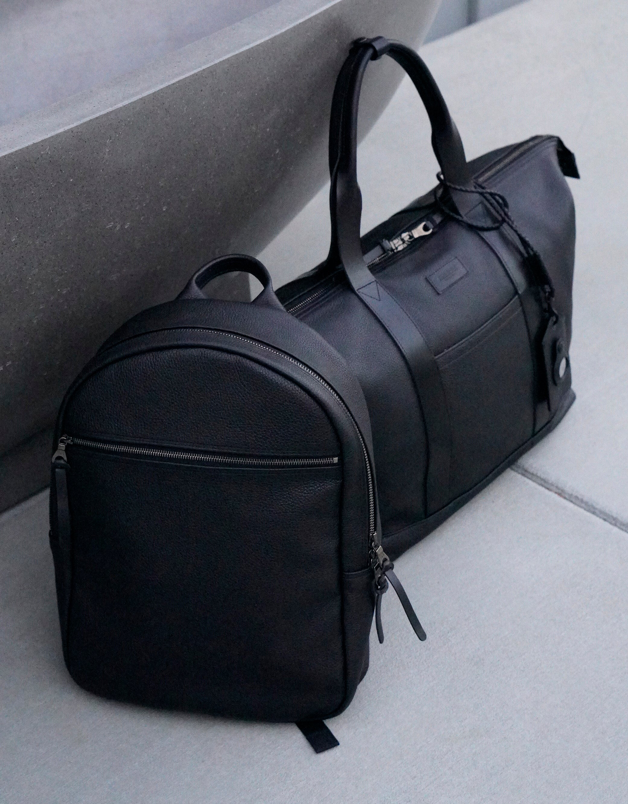 Black Leather Go Pack next to a Black Leather Travel Tote 2.0